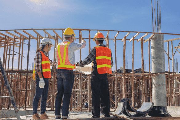 three construction workers looking over a project plan while on a busy worksite